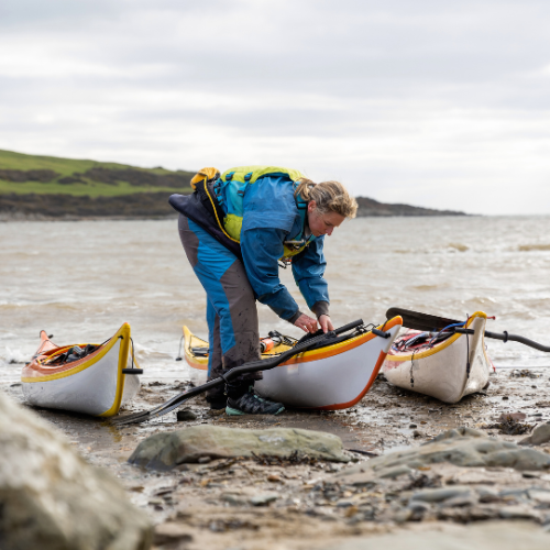 A woman wearing a drysuit preparing her kayak to go on the water.