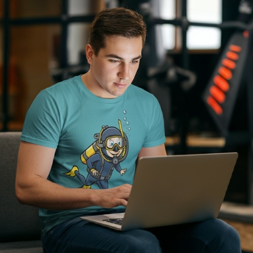 A man wearing a scuba diver t-shirt shopping on his laptop.