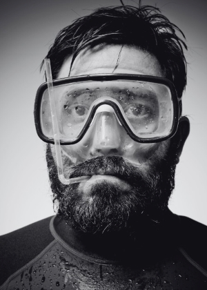 Beared man wearing a scuba mask. He has a straw in his mouth.