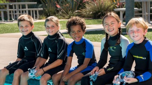 Five happy kids sitting at the edge of a pool