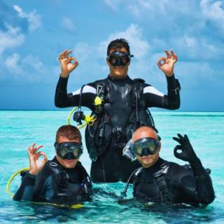 Three scuba divers above water making the OK gesture with their thumb and index fingers