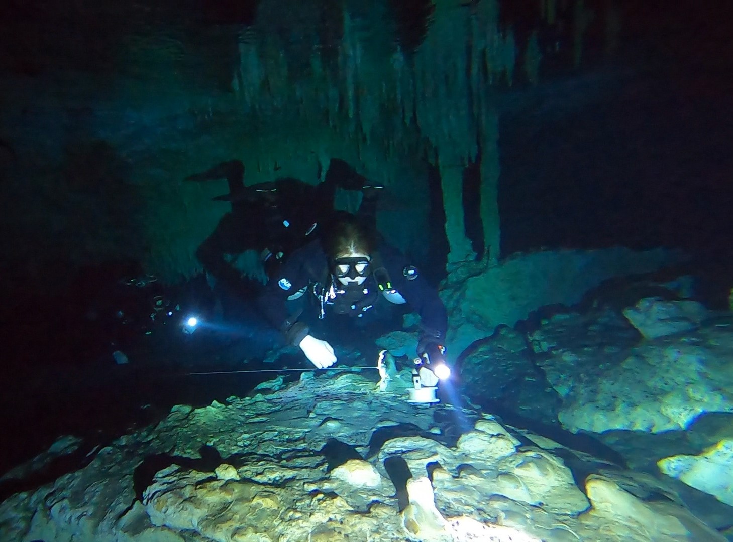 A sidemount diver in a cave underwater with lights illuminating his path