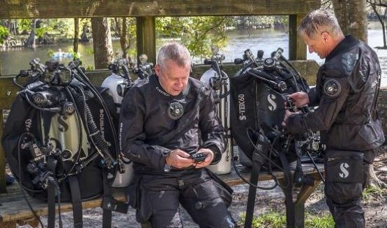 Two divers on a bench, adjusting their BCDs and other scuba gear