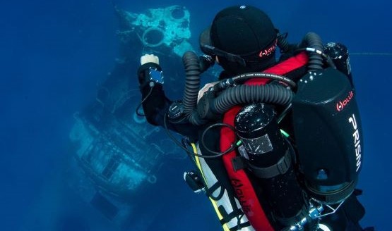 A technical diver underwater using a rebreather as he looks out at a shipwreck