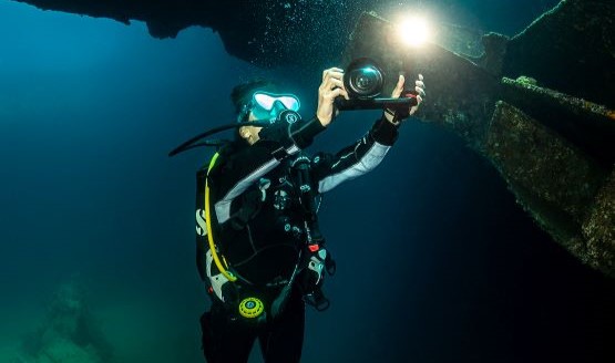 A diver is using an underwater camera to take a picture of a shipwreck