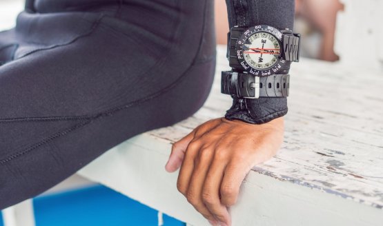 A dive compass around a diver's wrist. The diver is sitting on a bench.