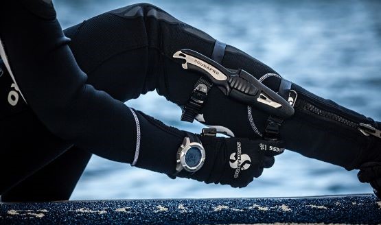 A diver sitting on a dock with a visible dive knife strapped on their boot