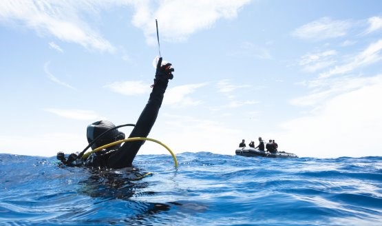 Diver holding a rescue beacon up in the water while a dive boat is off in the distance