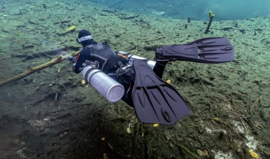 A sidemount diver underwater, shot from behind with his gear and fins visible.