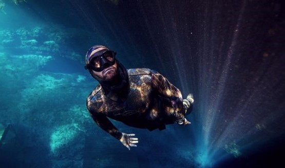 A freediver illuminate from behind with light. Wearing a black wetsuit and mask.