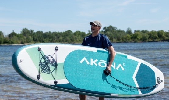 A man holding an inflatable paddle board on the edge of the water