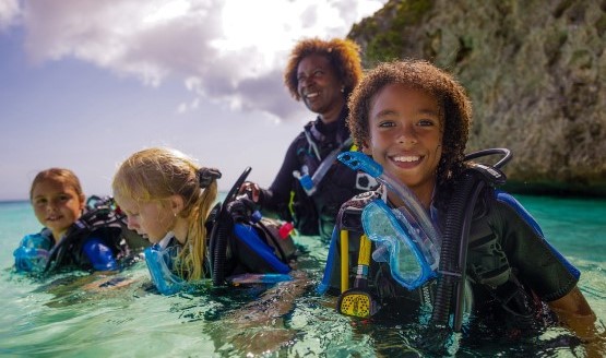 A smiling group of children wearing scuba gear. They're above water.