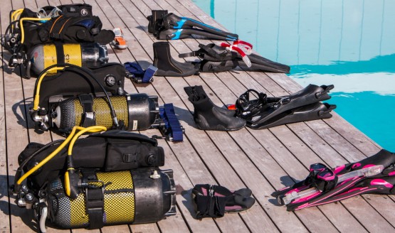 Several full sets of scuba gear including tanks, BCDs, fins, and masks are laid out on a dock.