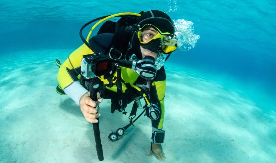 A diver underwater during the daytime with a camera mounted to a grip