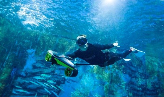 A diver, just below surface, using an underwater scooter around a rocky area