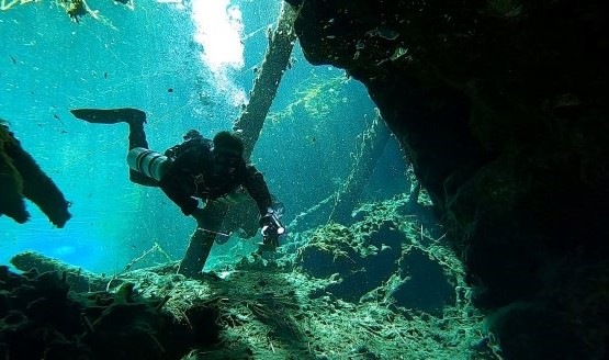 A diver is exploring a wreck underwater using a sidemount setup