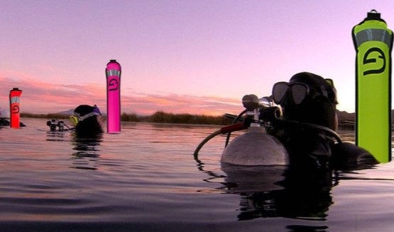 Two divers on the surface of the water with orange, pink, and yellow surface marker buoys