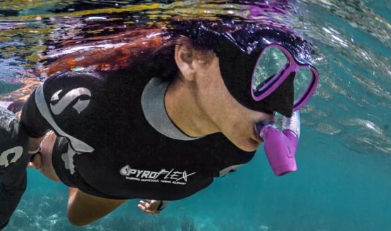 A woman snorkeling with a pink mask and snorkel wearing a black wetsuit